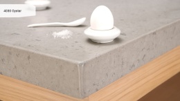 Caesarstone Oyster to elegancki konglomerat kwarcowy w odcieniach beżu i szarości, z charakterystycznymi ciemnymi inkluzjami