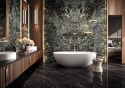 Łazienka z zielonym marmurem Verde France, wolnostojącą wanną i złotymi dodatkami oświetlenia.