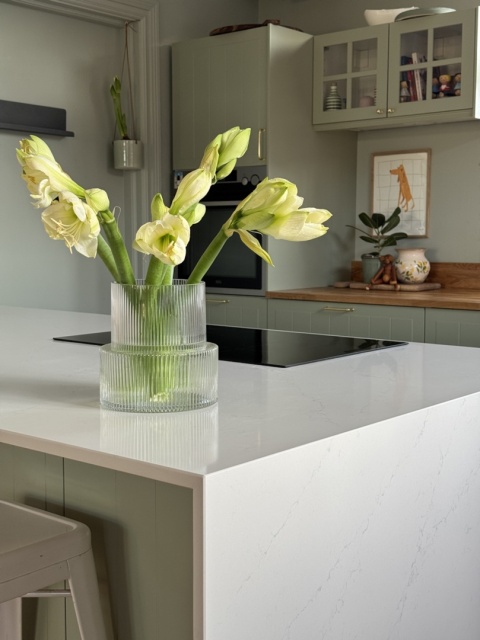 Wyspa kuchenna z białym blatem Silestone i zielonymi szafkami, dekoracja wazon z kwiatami