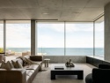 Minimalistyczny salon z panoramicznym widokiem na morze i betonowymi wykończeniami ścian.