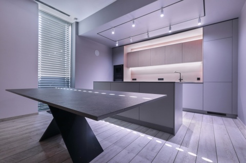 Minimalistyczna kuchnia z blatem w kolorze grafitowym, podkreślonym nowoczesnym oświetleniem