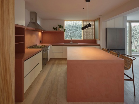 Nowoczesna kuchnia z wyspą i blatami w odcieniu ceglastym, z naturalnym oświetleniem i drewnianą podłogą.