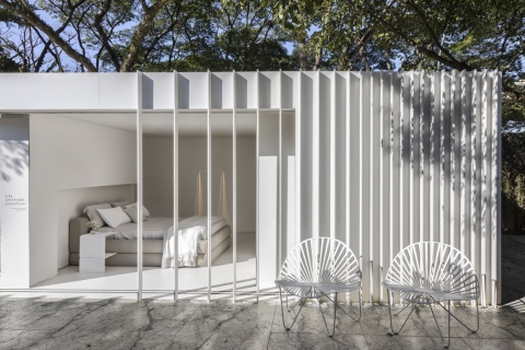 ypialnia z białymi panelami Dekton Zenith – minimalistyczne wnętrze z łóżkiem w jasnej tonacji i okładziną ścienną.