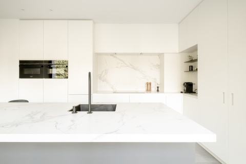 Kuchnia z wyspą i białym blatem Dekton Zenith – nowoczesne wnętrze z kontrastującym czarnym kranem.