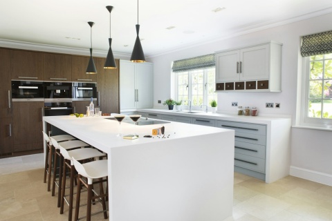 Elegancka kuchnia z dużą wyspą – biały blat i zabudowa Dekton Zenith połączone z drewnianymi szafkami.