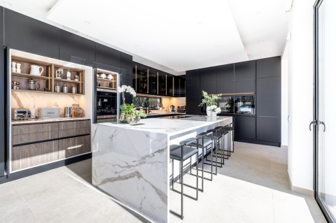 Przestronna kuchnia z wyspą i czarnymi szafkami, kontrastującymi z blatem Vigil kC poler, eksponującym złote i szare żyły.