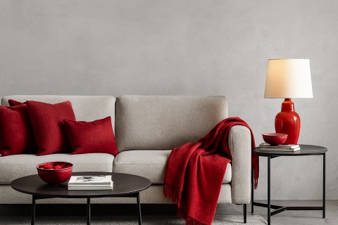 Spiek Titan Cemento jako ściana akcentująca, jasna sofa, czerwone dodatki i poduszki, neutralne światło