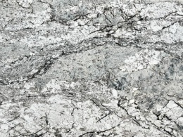 zbliżenie powierzchni kamienia, ukazujące kontrastowe przejścia barw i drobne akcenty brązu lub beżu na tle granitu.