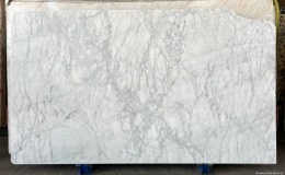 Płyta marmuru Bianco Carrara C szlif, jasne tło z wyraźniejszym, pionowym szarym użyleniem.