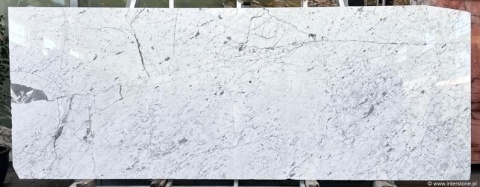 Szeroka płyta marmuru Bianco Carrara C, prawie białe tło z gęstym, drobnym szarym użyleniem.