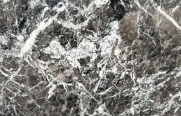 Zbliżenie marmuru Grigio Carnico, ciemnoszara struktura z nieregularnymi białymi żyłkami i krystalicznymi fragmentami.