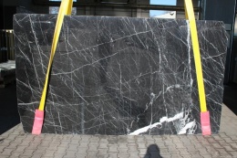 Płyta marmuru Nero Marquina, czarne tło z gęstą siecią cienkich białych żył, ustawiona pionowo.