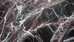 Marmur Rosso Levanto, ciemnoczerwone tło z intensywnymi białymi żyłkami i kontrastowymi czarnymi fragmentami.