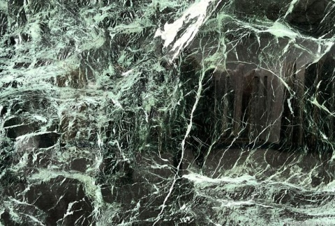 Detal płyty marmuru Verde Tinos, gęste jasne żyły na ciemnozielonym tle, wykończenie na wysoki połysk