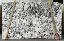 Płyta granitu Orion White, jasne tło z ciemnym, nieregularnym użyleniem, widok całej tafli w hali