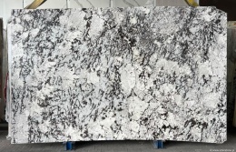 Płyta granitu Orion White, jasne tło z ciemnym, nieregularnym użyleniem, widok całej tafli w hali