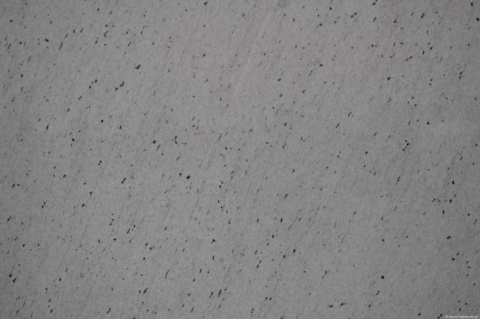 Zbliżenie granitu Perfect White poler, białe tło z gęstymi, ciemnymi drobinkami układającymi się diagonalnie