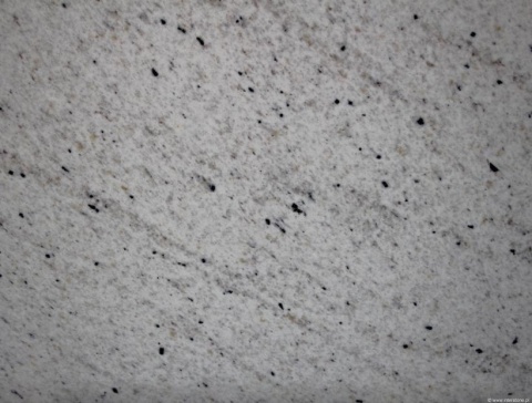 Detal granitu Perfect White poler, jasna powierzchnia z licznymi ciemnymi inkluzjami i lekkim efektem chmurzenia