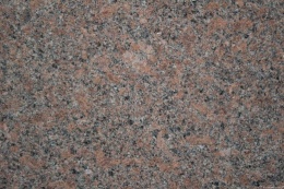Zbliżenie granitu Santiago Red płomień, drobnoziarnista czerwonawo-szara struktura z ciemnymi wtrąceniami