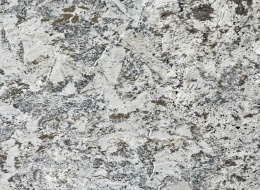 Zbliżenie granitu Siberian White poler, jasne tło z nieregularnymi szaro-brązowymi plamami i kontrastową strukturą