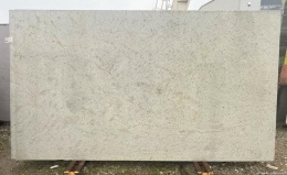 Płyta granitu Spring White ustawiona pionowo na zewnątrz – jasny kamień o subtelnym, nakrapianym wzorze.