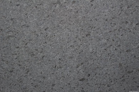 Zbliżenie granitu Steel Grey płomień – szary, drobnoziarnisty wzór i chropowata faktura płomieniowana.