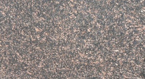 Zbliżenie granitu Tan Brown płomień – drobnoziarnista struktura z brązowymi wtrąceniami, faktura płomieniowana.