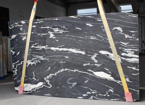 Granit Titanium Black – duża płyta z dynamicznym białym użyleniem; widoczne pasy transportowe w hali.