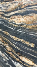 Zbliżenie granitu Titanium Gold – ciemne tło z falującymi żyłami w odcieniach złota, beżu i bieli.