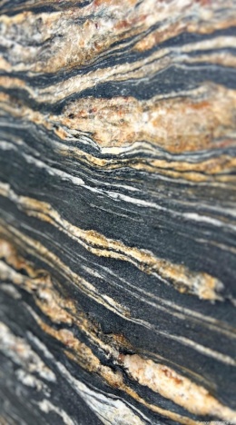 Zbliżenie granitu Titanium Gold – ciemne tło z falującymi żyłami w odcieniach złota, beżu i bieli.