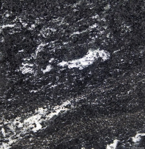 Zbliżenie granitu Via Lattea – ciemna, ziarnista struktura z białymi przeżyleniami i jasnymi wtrąceniami.