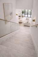 Nowoczesne schody ze spieku kwarcowego Marazzi Concrete Look Ivory prowadzące z piętra mieszkania do jasnego salonu.