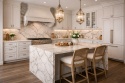 Kuchnia w stylu neoklasycznym z wyspą i blatami ze spieku Fusion White, jasna zabudowa i złote detale.