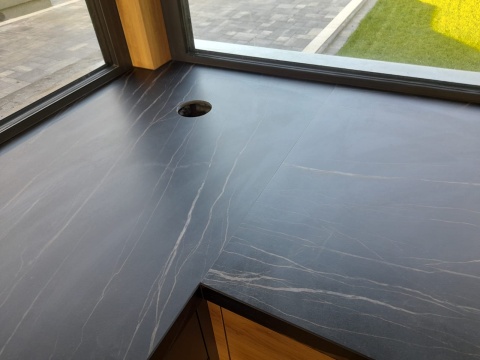 Blat kuchenny ze spieku Noir Desir z delikatnym złotym użyleniem, nowoczesna zabudowa z drewnianymi frontami.