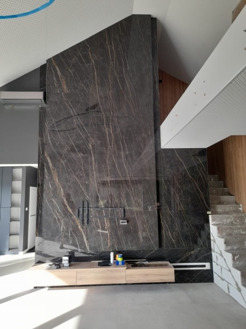 Ściana TV ze spieku Noir Desir z pionowym użyleniem, nowoczesne wnętrze z antresolą i drewnianymi elementami.