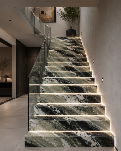 Schody wykończone Jade Green z podświetleniem LED i szklaną balustradą w nowoczesnym wnętrzu.