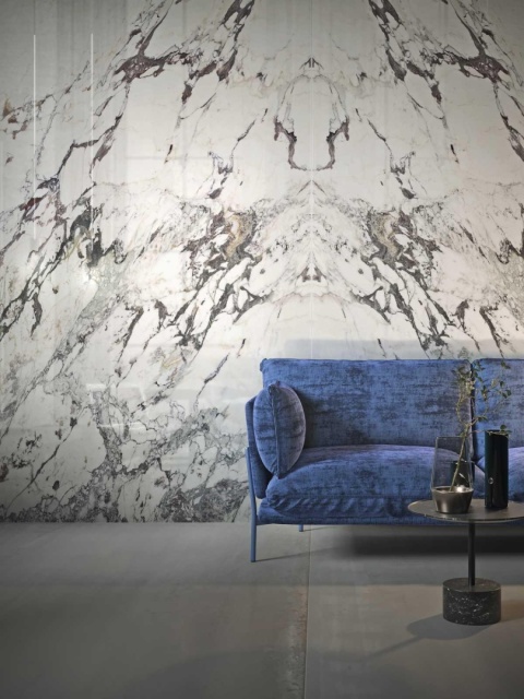 Marazzi Capraia Lux na dekoracyjnej ścianie salonu z niebieską sofą i ciemną, nowoczesną posadzką