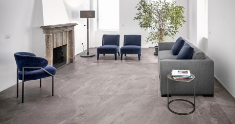 Posadzka Marazzi Ardesia Cenere 120 × 120 cm w eleganckim salonie z kominkiem, granatowymi fotelami i szarą sofą