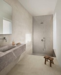 Jasne płytki Marazzi Cementum Ash w minimalistycznej łazience z prysznicem i kamienną umywalką