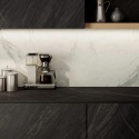 Nowoczesna kuchnia z ciemnymi powierzchniami Marazzi Bahia Black zestawionymi z jasną, marmurową okładziną ścienną