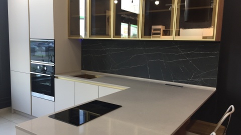 Kuchnia z jasnym blatem TechniStone Noble Ivory White i czarnym dekoracyjnym panelem ściennym.