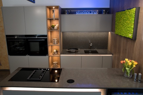 Kuchnia z blatem TechniStone Noble Pietra Grey Poler, czarną zabudową i naturalnym drewnem.