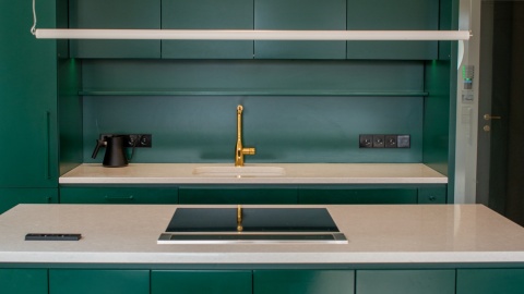 Jasny blat TechniStone Noble Quartzite w kuchni z zieloną zabudową i złotą armaturą.