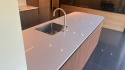 Wyspa kuchenna z jasnym blatem TechniStone Starlight White i drewnianą zabudową.