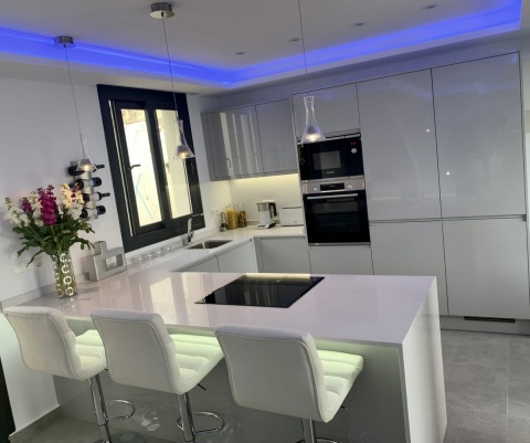 Kuchnia z wyspą TechniStone Starlight White i jasną zabudową na wysoki połysk.