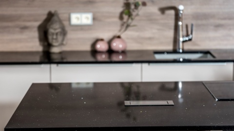 Czarny blat TechniStone Starlight Black w kuchni z jasnymi frontami i drewnianą ścianą.