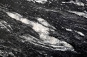 Zbliżenie granitu Cosmic Black szczotkowanego z czarną bazą i szerokimi kremowo-białymi pasmami.