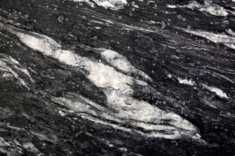 Zbliżenie granitu Cosmic Black szczotkowanego z czarną bazą i szerokimi kremowo-białymi pasmami.