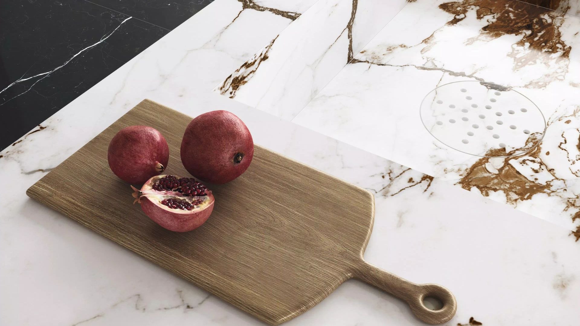  Deska do krojenia z granatami na blacie kuchennym wykonanym ze spieku Marble Capraia od Florim Stone. Jasna powierzchnia z ciemnobrązowym żyłkowaniem i zintegrowanym zlewem w tle.