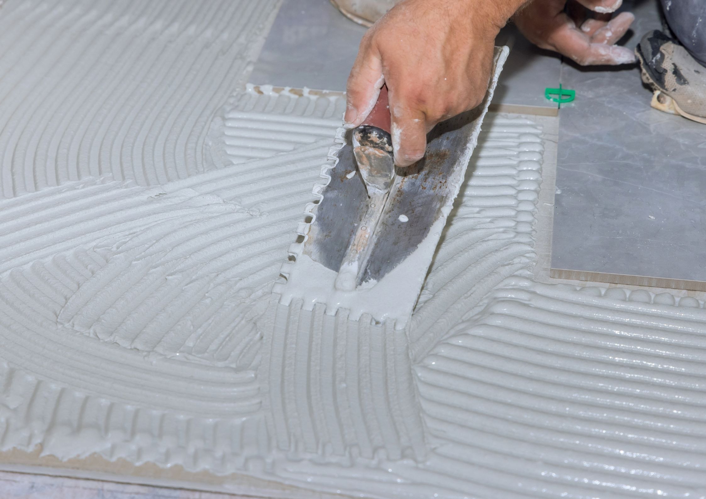 Ręka pracownika rozprowadza klej montażowy pacą zębatą na posadzce – przygotowanie pod spieki lub płytki